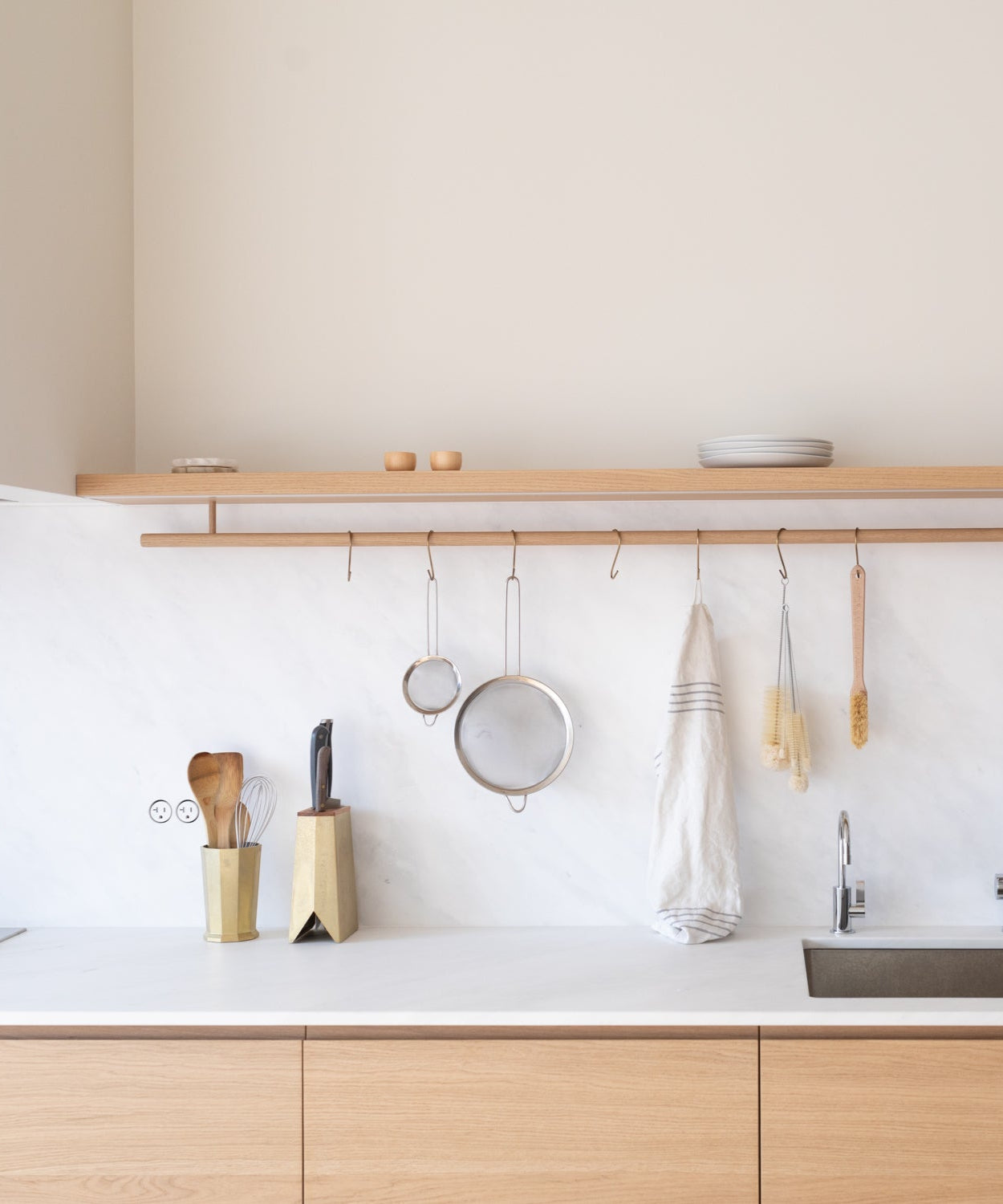 Modern kitchen with wooden cabinets, discrete flush Bocci outlets, white countertop, and hanging kitchen utensils.