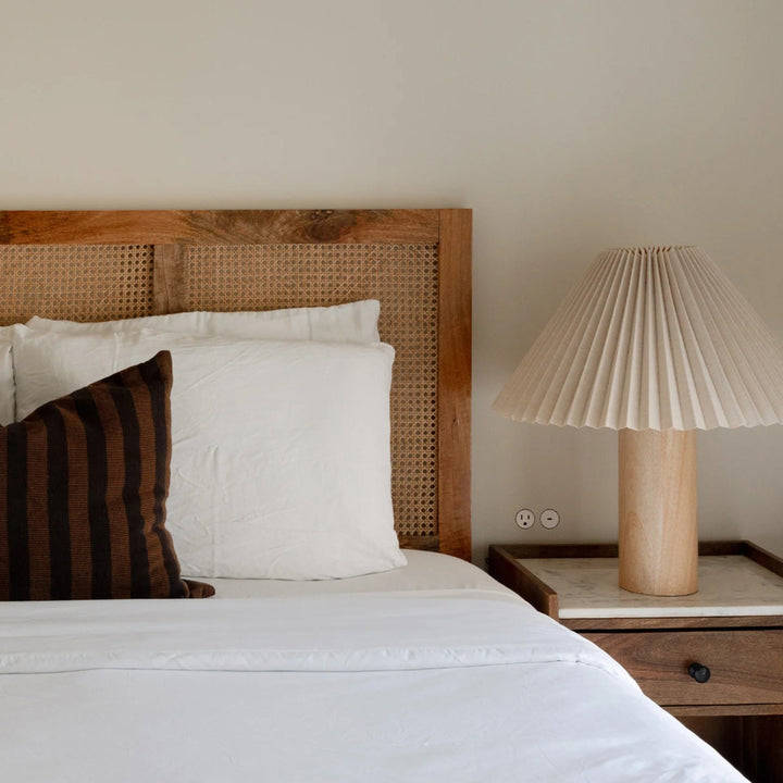 Bedroom with wooden cane headboard, white bedding, and a pleated lamp on a nightstand with discrete Bocci 22 bedside flush outlets.
