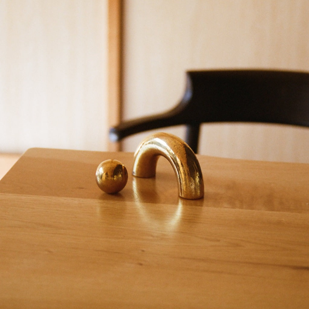 Brass Maha Alavi Cercle knob and arc pull on a wood table.