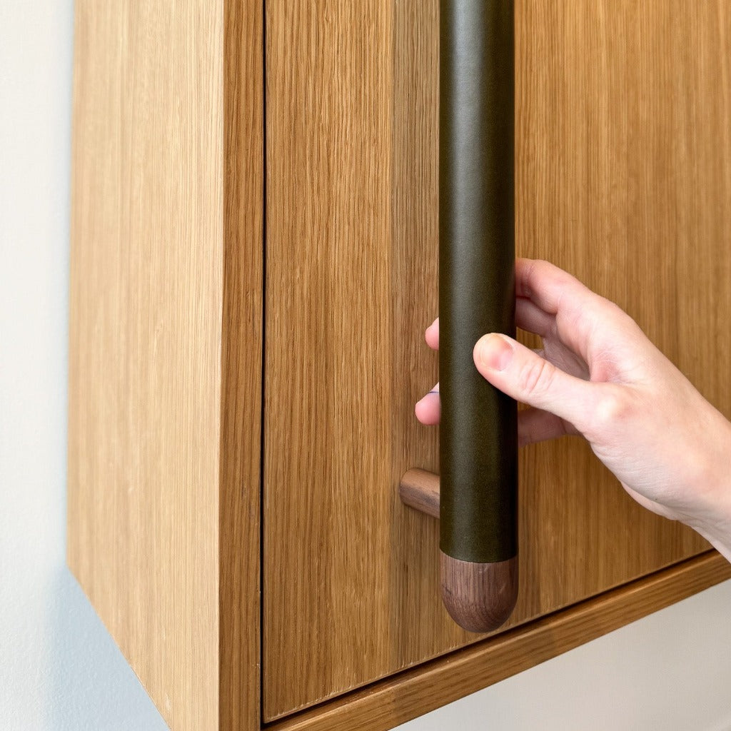 A wood and leather Chapman & Bose appliance bar pull on a cabinet.