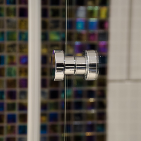 A close up of a glass door with a Baccman Berglund Dot Shower Door Knob.
