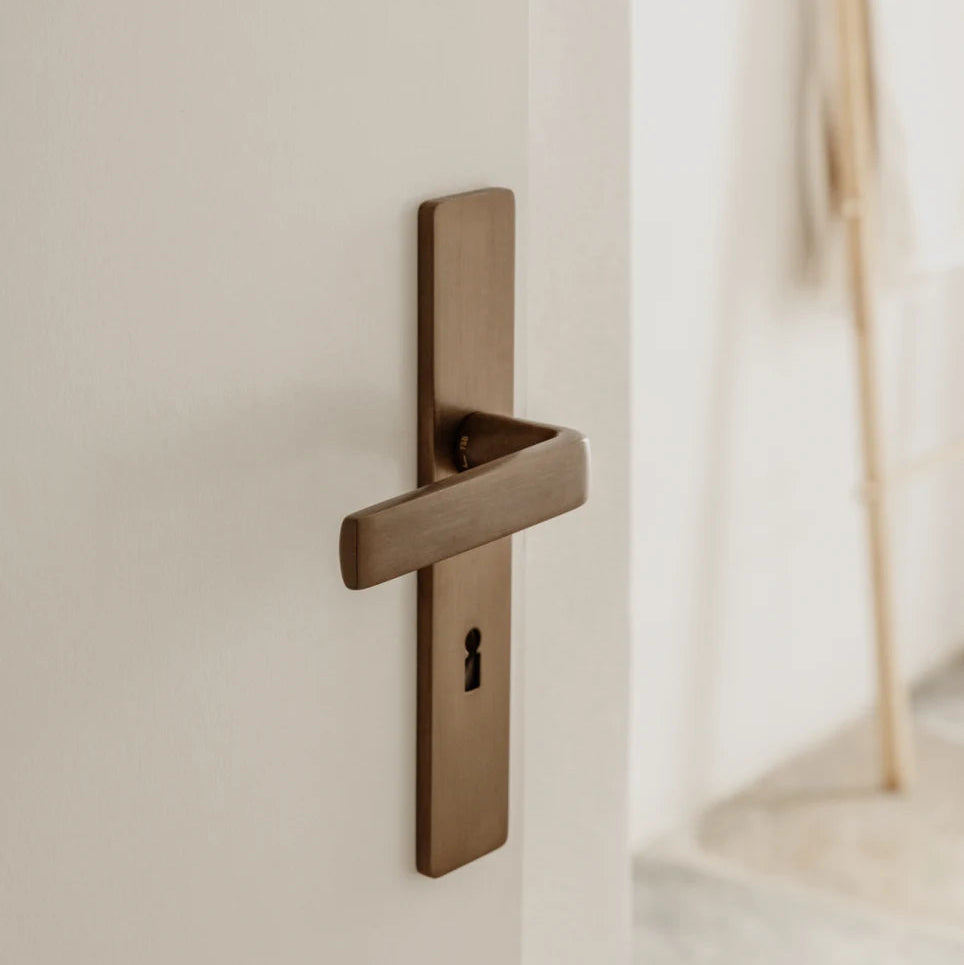 FSB 1267 lever and escutcheon at Piperi House, Kythnos, showing the flat-grip form against a plaster wall.