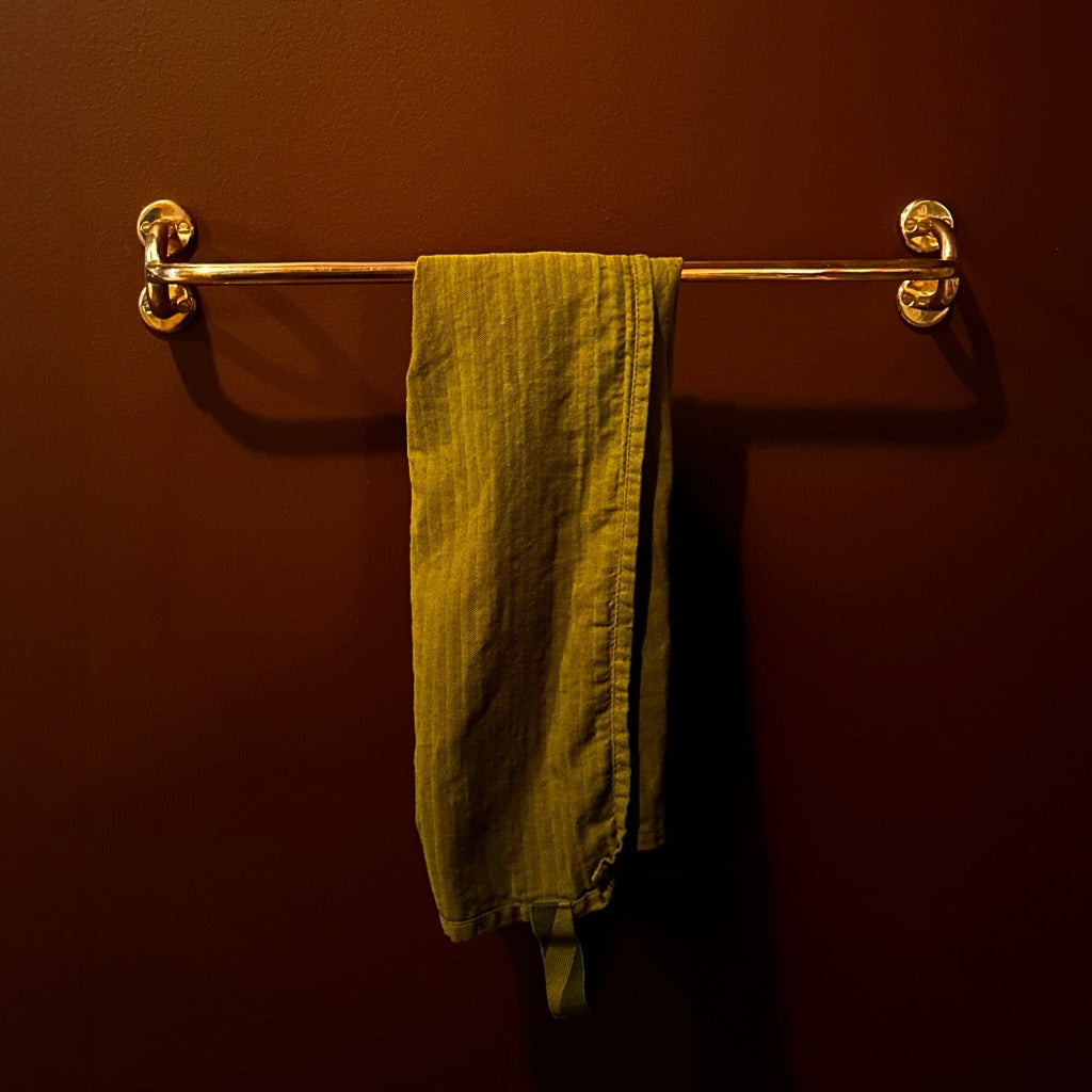 Brass Maha Alavi Fauna towel bar with a yellow towel in a dark room.
