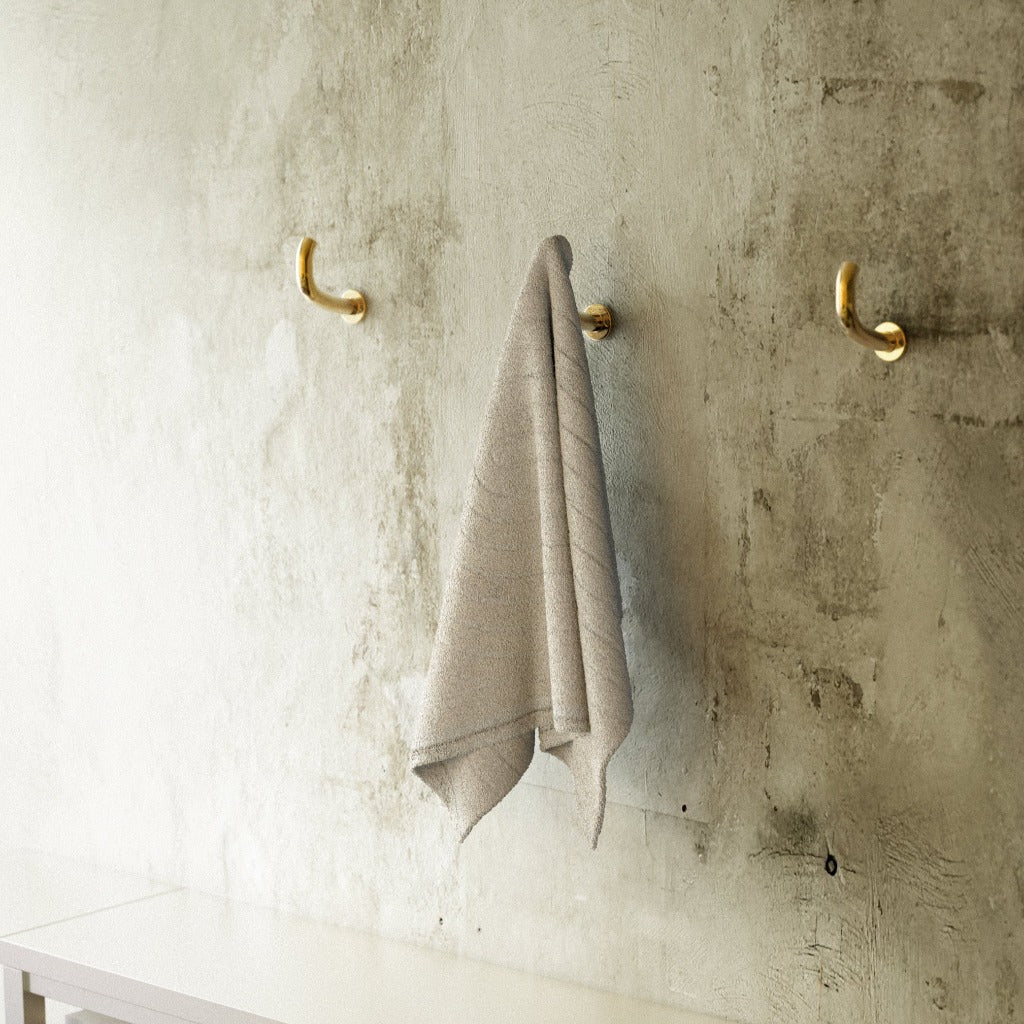 Brass Maha Alavi Fauna wall hooks with a towel on a concrete wall.