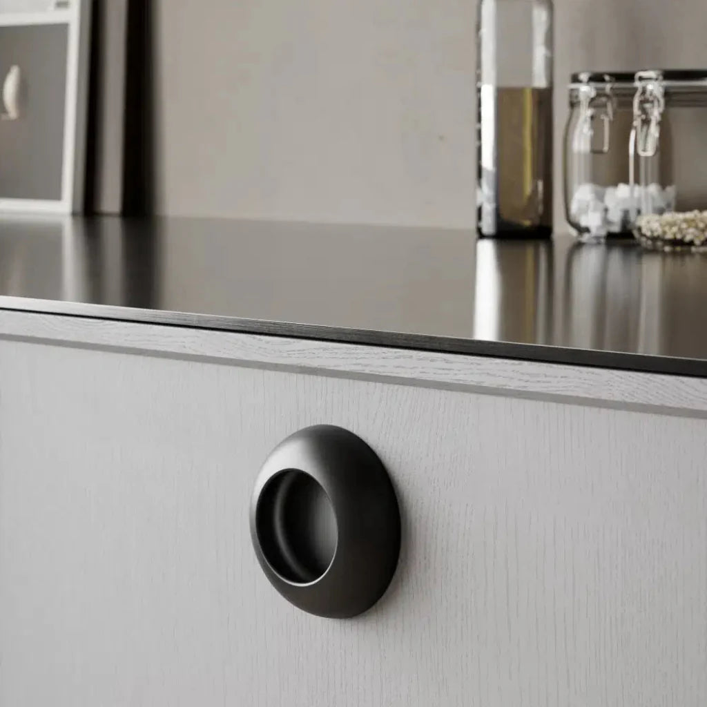 Black cup-style cabinet knob mounted on white drawer