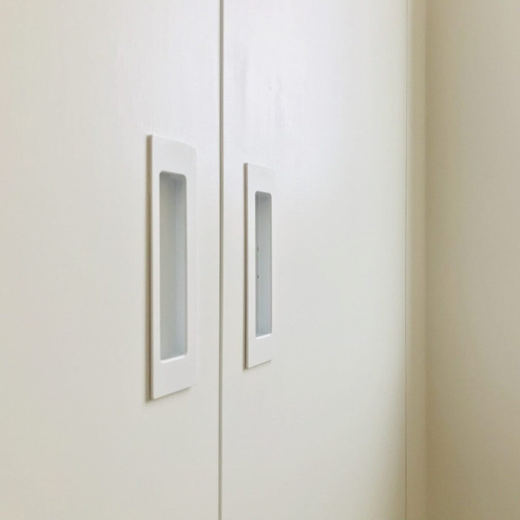 Pair of white HB 675 bi-fold flush pulls installed in white cabinet doors.