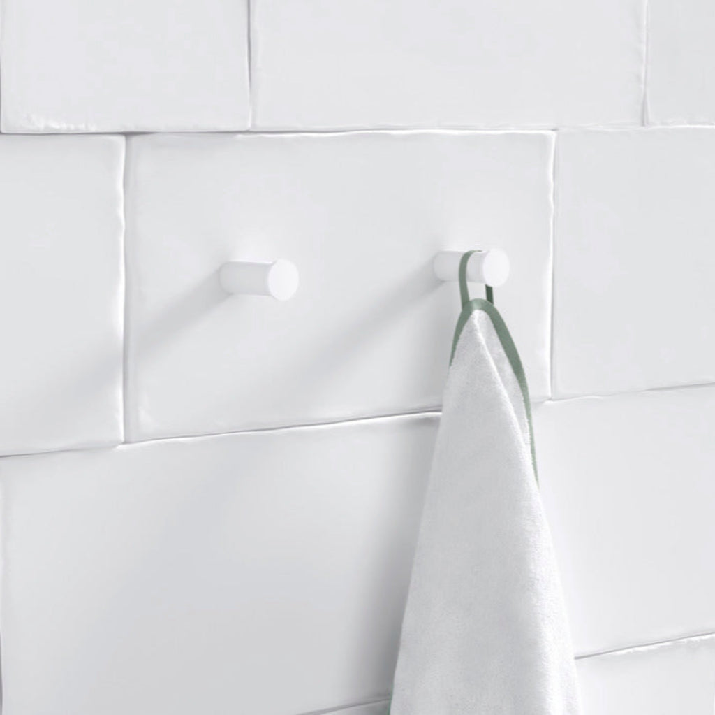 A white-tiled wall with a Hewi hook holding a towel.