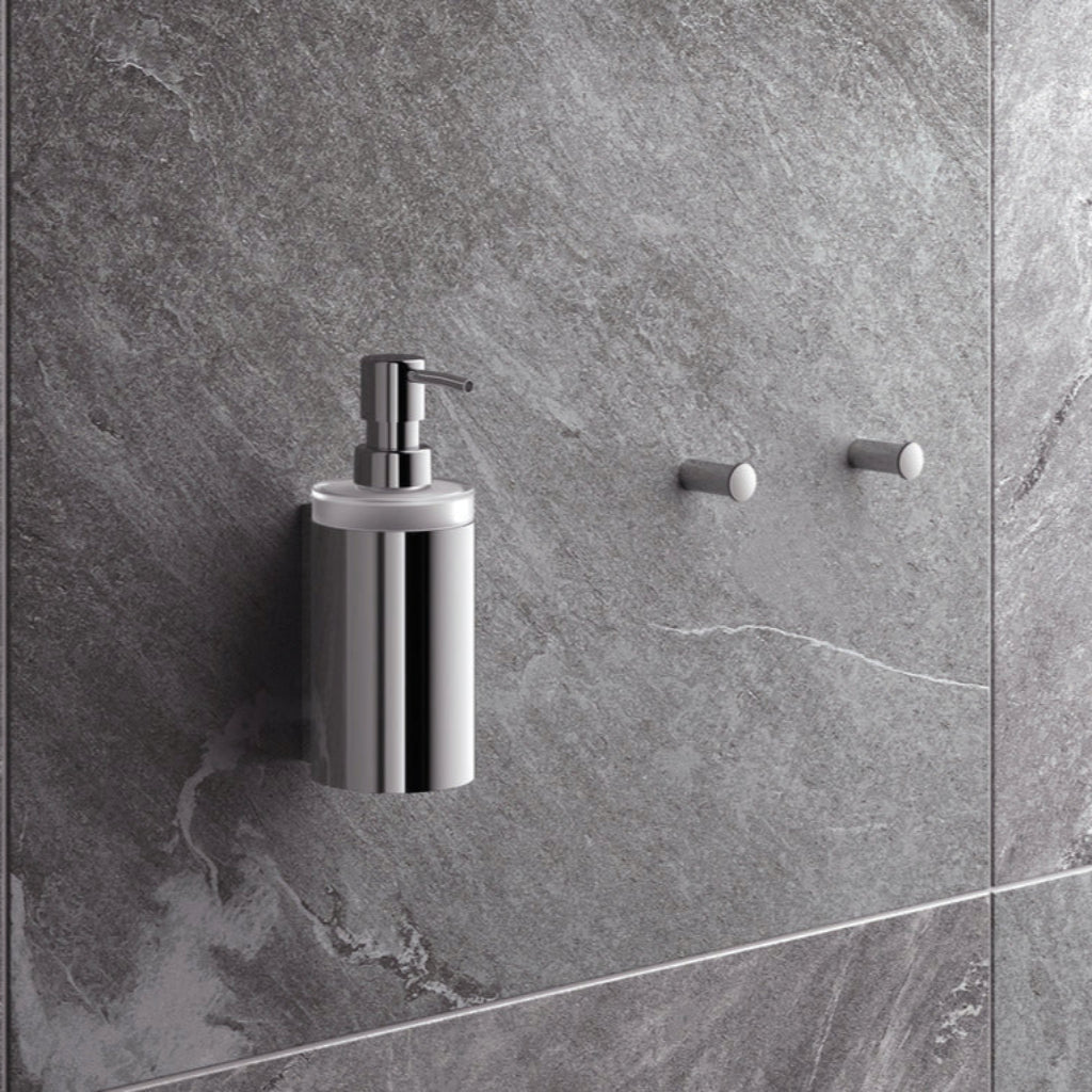 Polished chrome Hewi 900 soap dispenser on a grey stone wall.