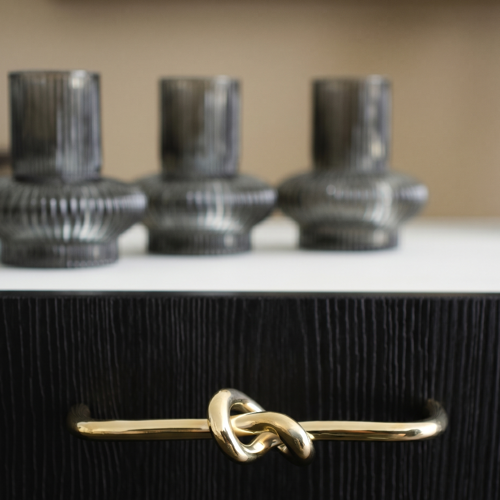 Gold knot handle on a dark wooden drawer with blurred glass containers in the background.
