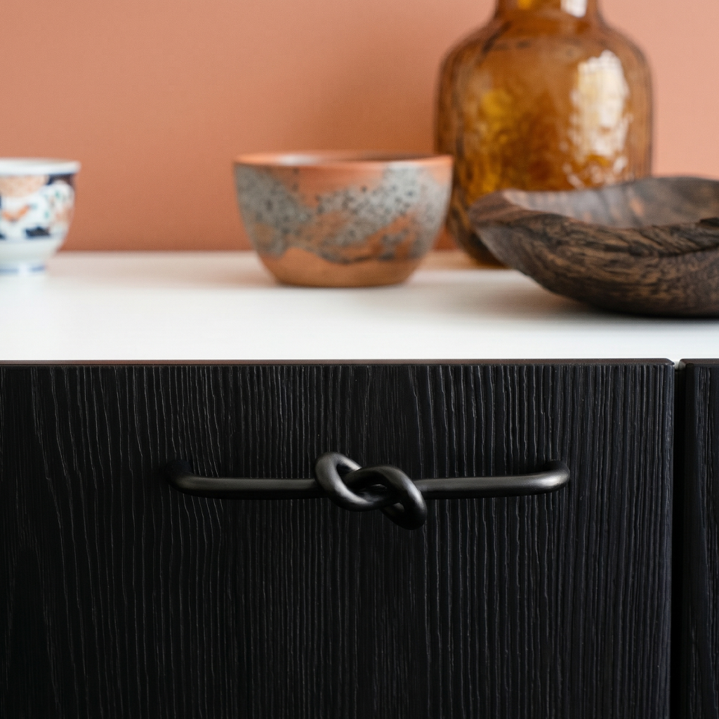 Black cabinet with a handle, white countertop, and ceramic bowls on a peach-colored wall.