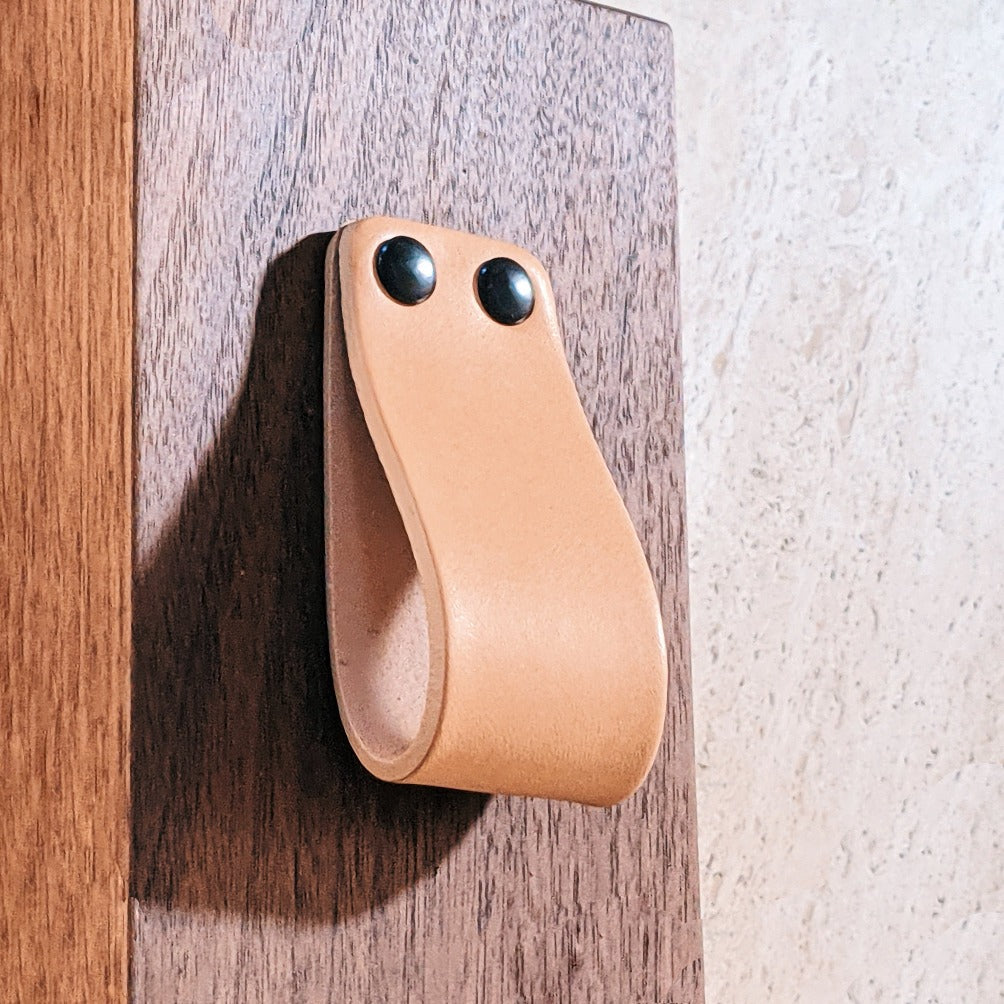 natural vegetable tanned leather loop cabinet pull with 2 black capped fasteners mounted on walnut wood from Chapman and Bose