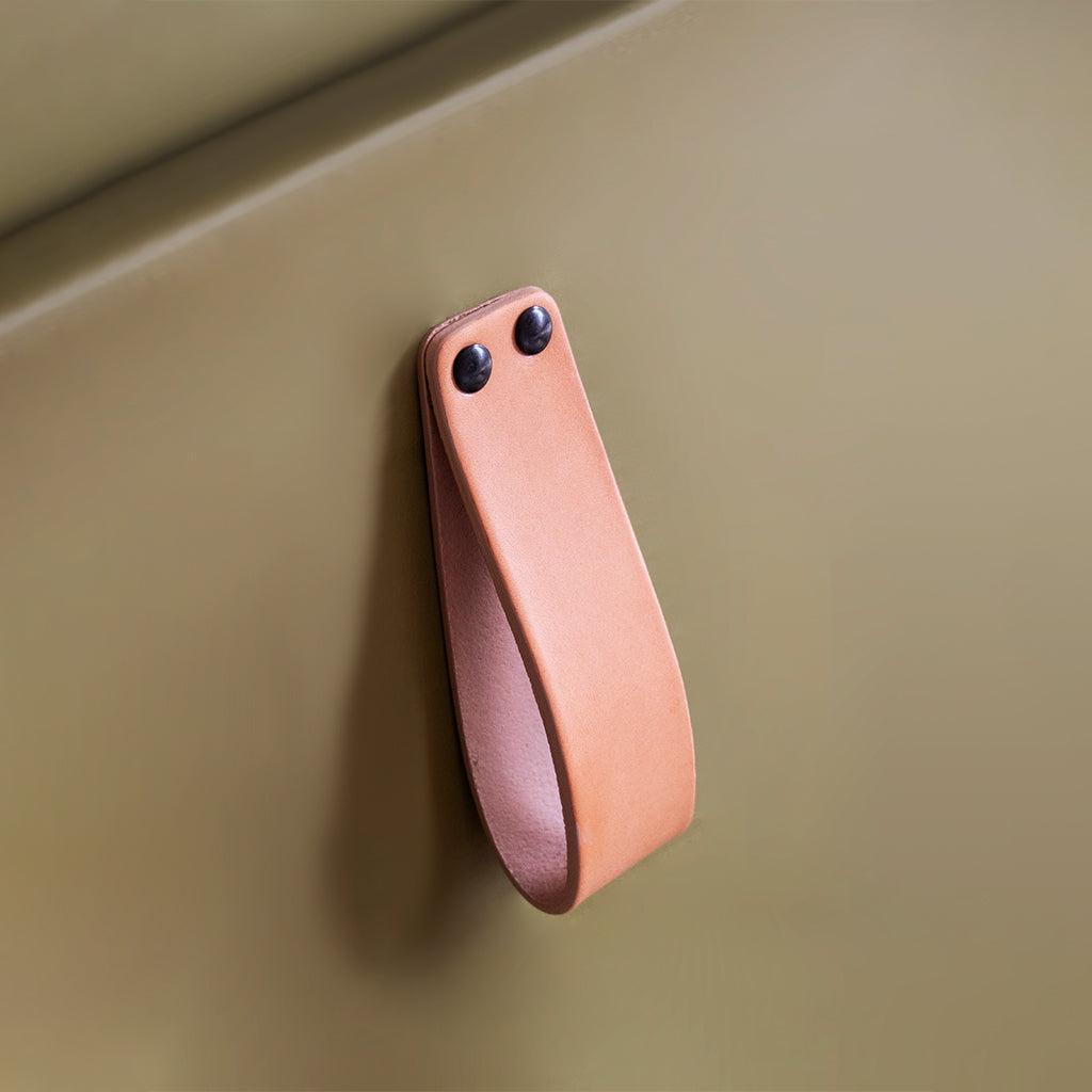 natural vegetable tanned leather loop cabinet pull with 2 black capped fasteners mounted on green cabinet from Chapman and Bose