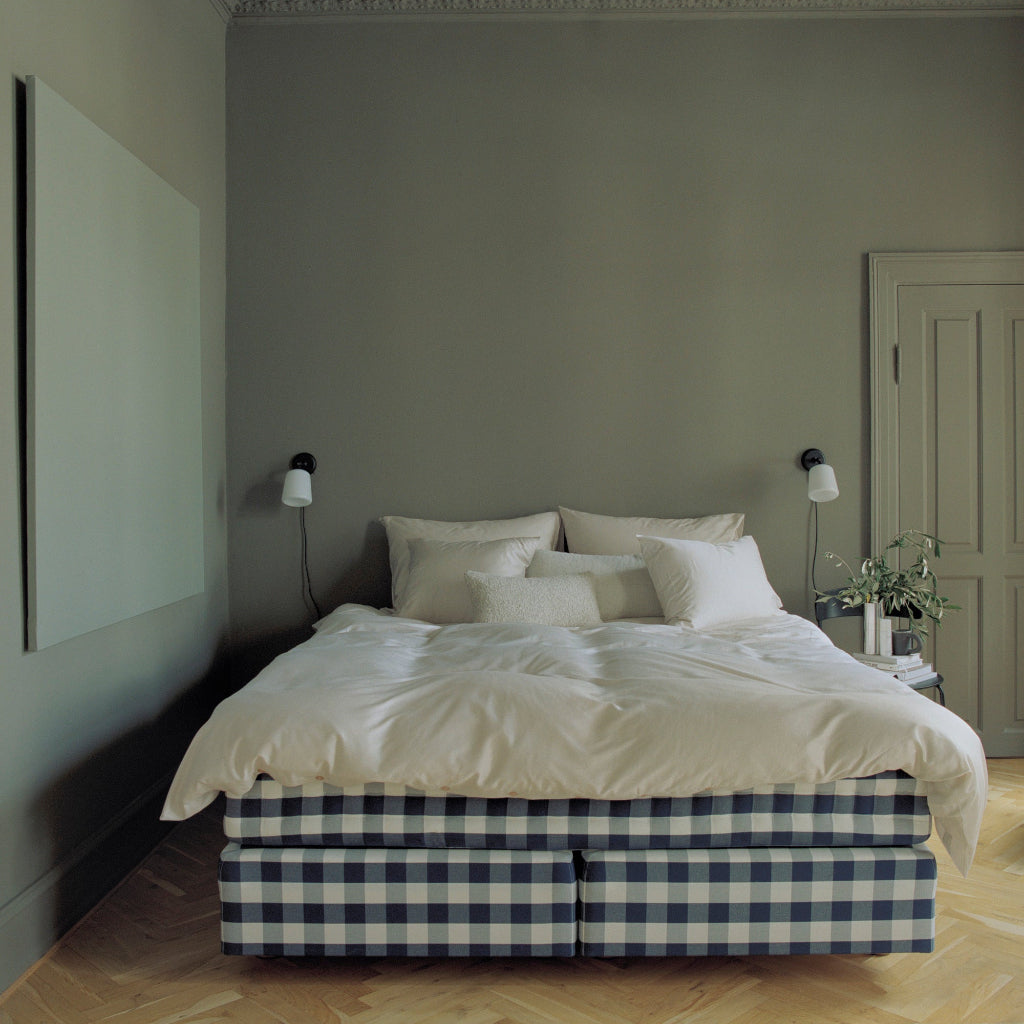 Minimalist white wall lamps with black frames mounted above a bed in a modern bedroom with sage green walls.
