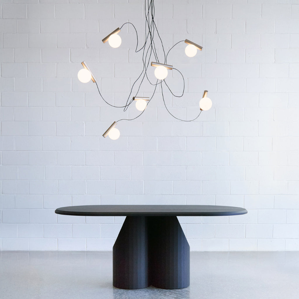 Modern black dining table with a unique base design under a stylish chandelier against a white wall.