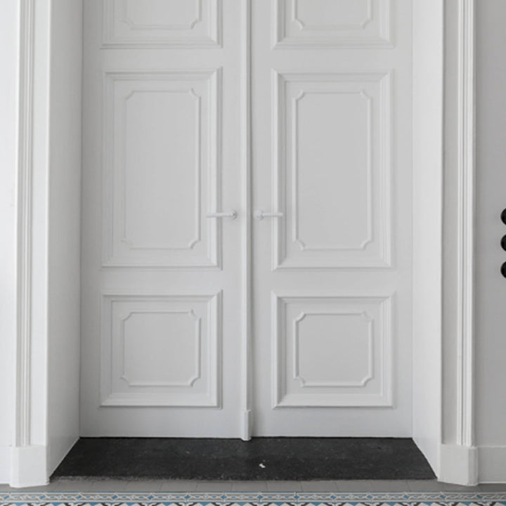 A cat sitting on the floor in front of a white Formani ONE by Piet Boon Door Lever.