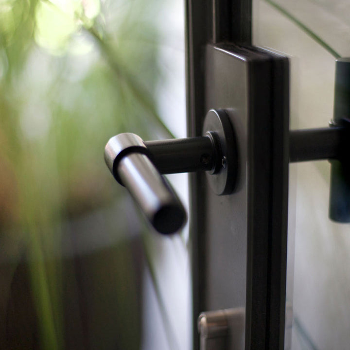 A close up of a Formani ONE by Piet Boon Door Lever with a plant in the background.