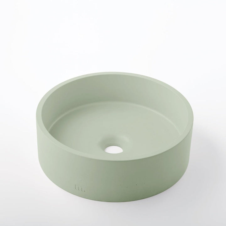 A round green Odet Basin SM sink on a white mudd. concrete surface.