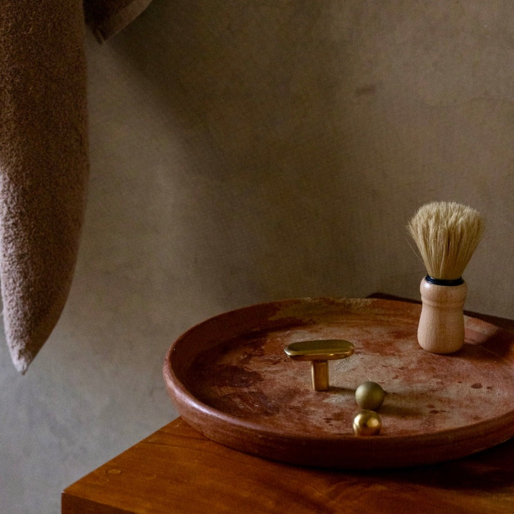 Brass Maha Alavi Oval knob styled on a wood tray in a bathroom.