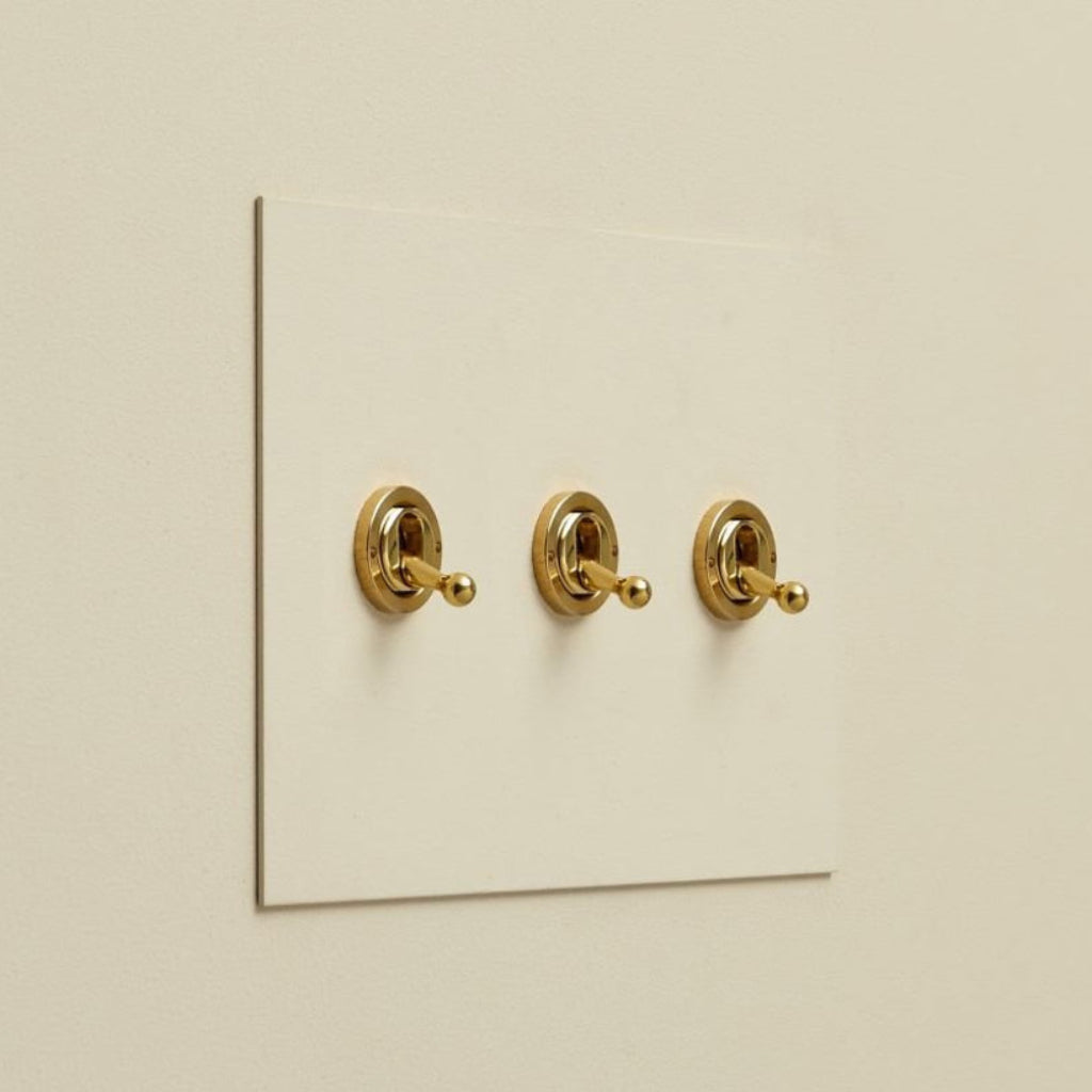 Cream Forbes & Lomax painted switch plate with three brass toggle switches.