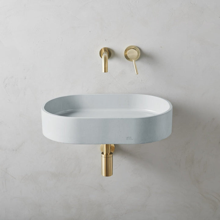 A mudd. concrete Parro Basin LG Affix with a gold faucet and a white wall.