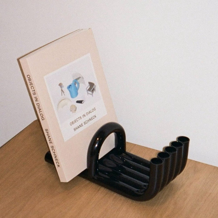 Black TUBE Bookends photographed on a wood table in a white room with a collection of books in between