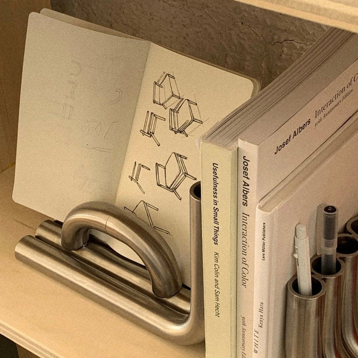 Black TUBE Bookends photographed on a wood table in a white room with a collection of books, notes and pens compartmentalized into sections of the object