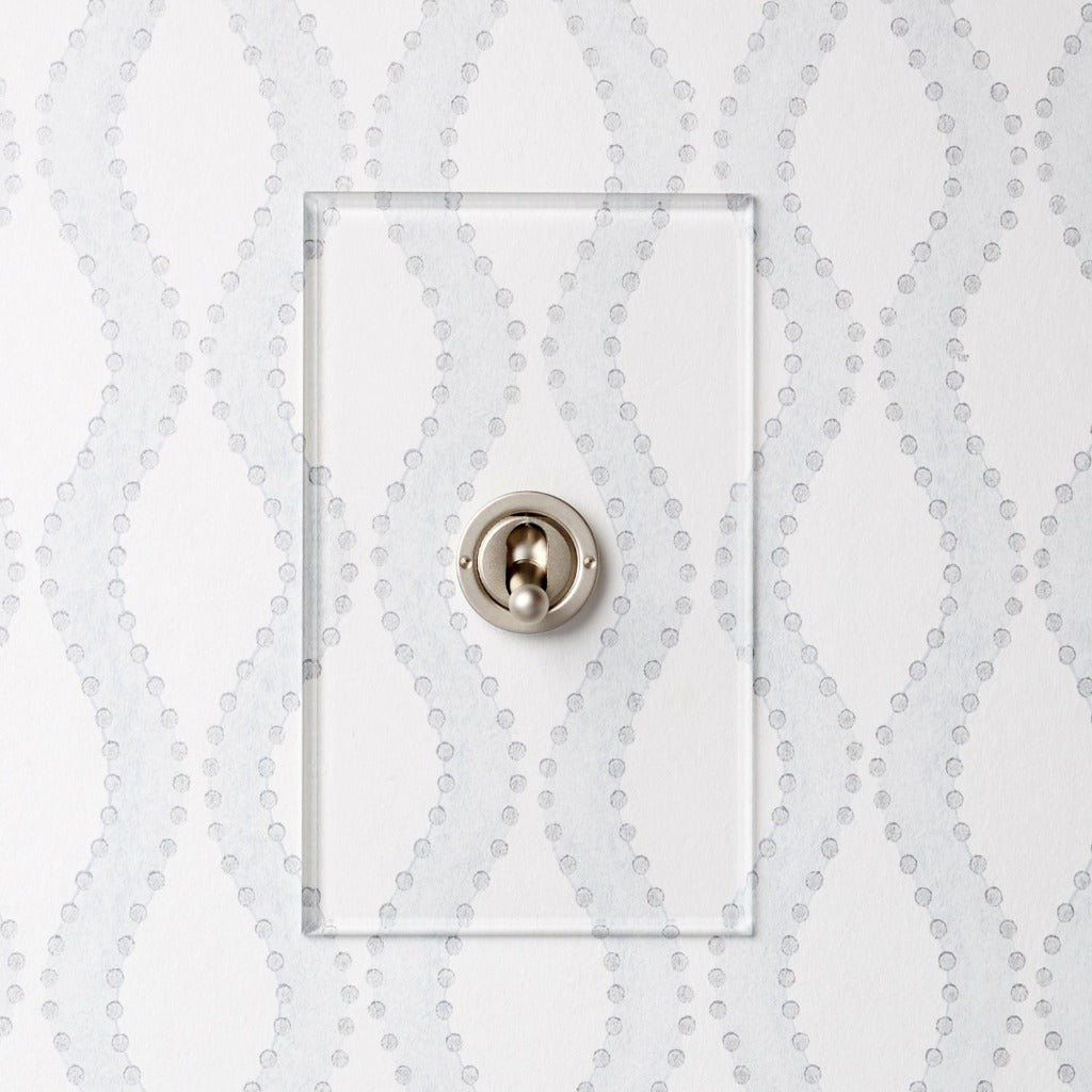 Forbes & Lomax invisible plate toggle switch against patterned wallpaper.