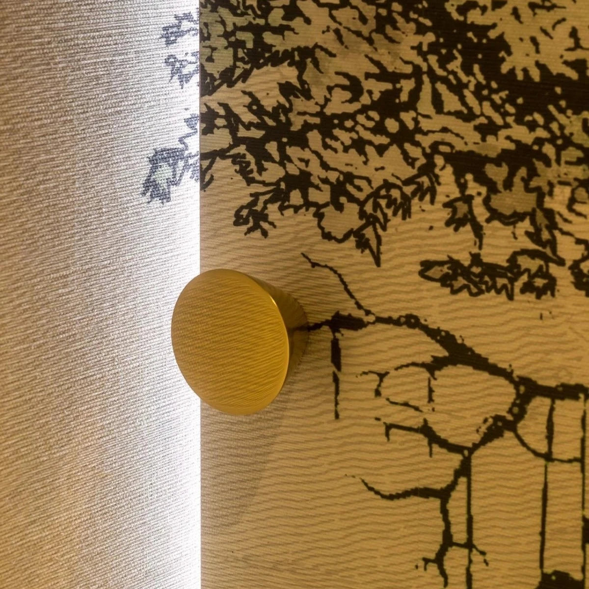 Brass Vervloet Audrey knob on a wall with a tree-shadow mural.