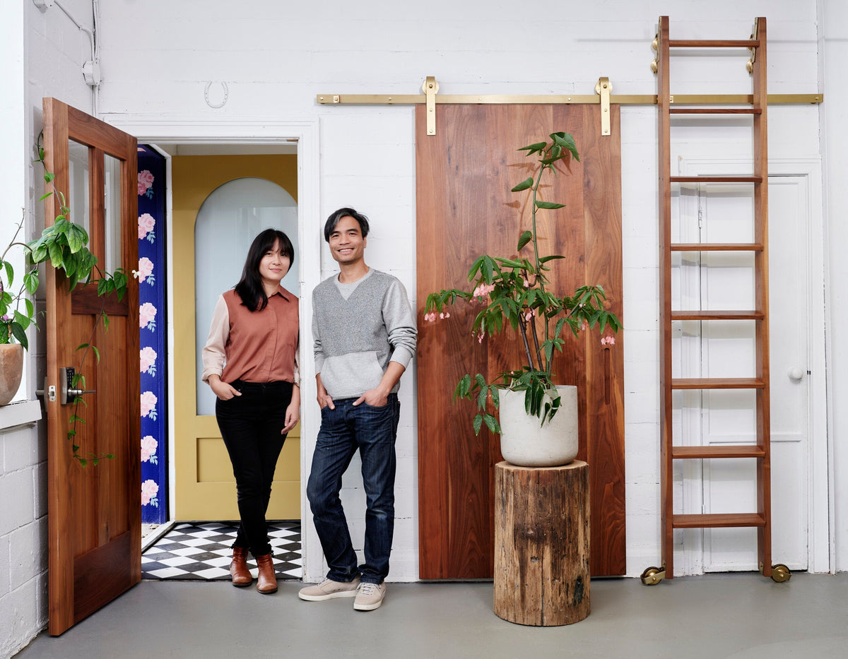 Husband and Wife team behind 1925workbench stand in front of brassy beau barn door