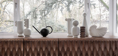White and black sculptural vases sitting on a wood table in front of a window
