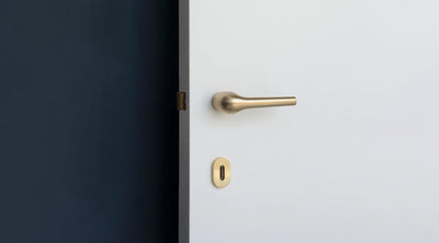 Minimal and organic Brass Door Lever and lock on a white door panel.