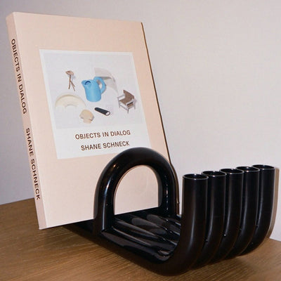 Black TUBE Bookends photographed on a wood table in a white room with a collection of books in between
