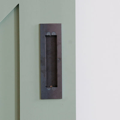 A 1925Workbench Flush Door Pull on the side of a green door.