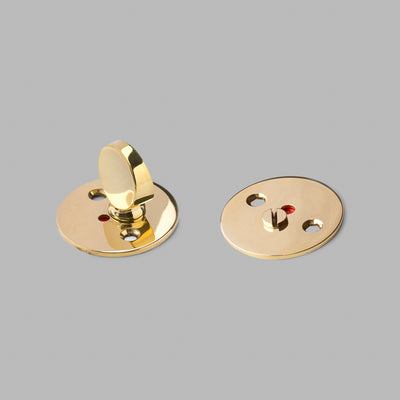 A pair of Arne Jacobsen Toilet Indicator buttons from d line, gold-plated, on a gray background.