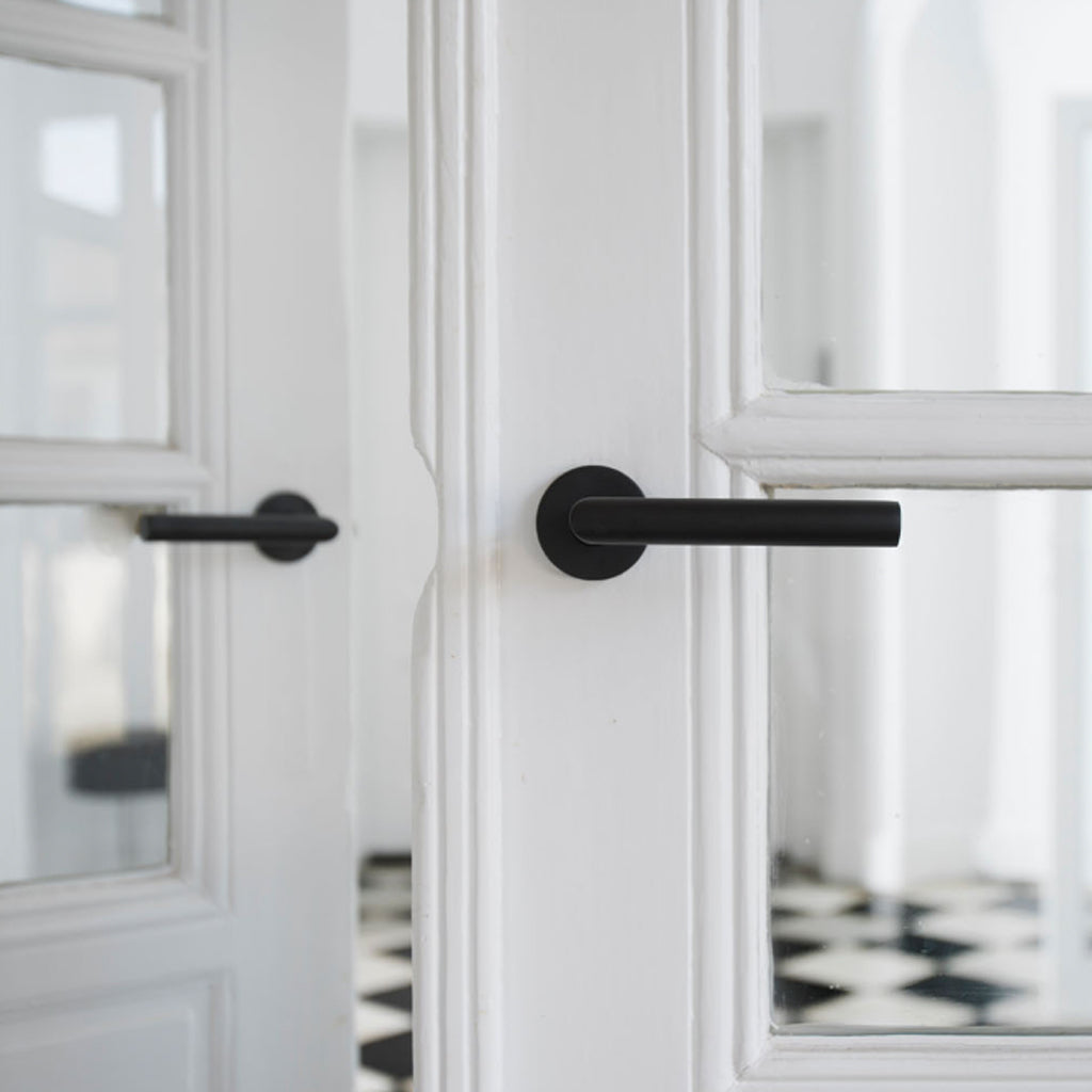 A pair of Formani BASICS LBIII-19 Door Levers in black on a white door.