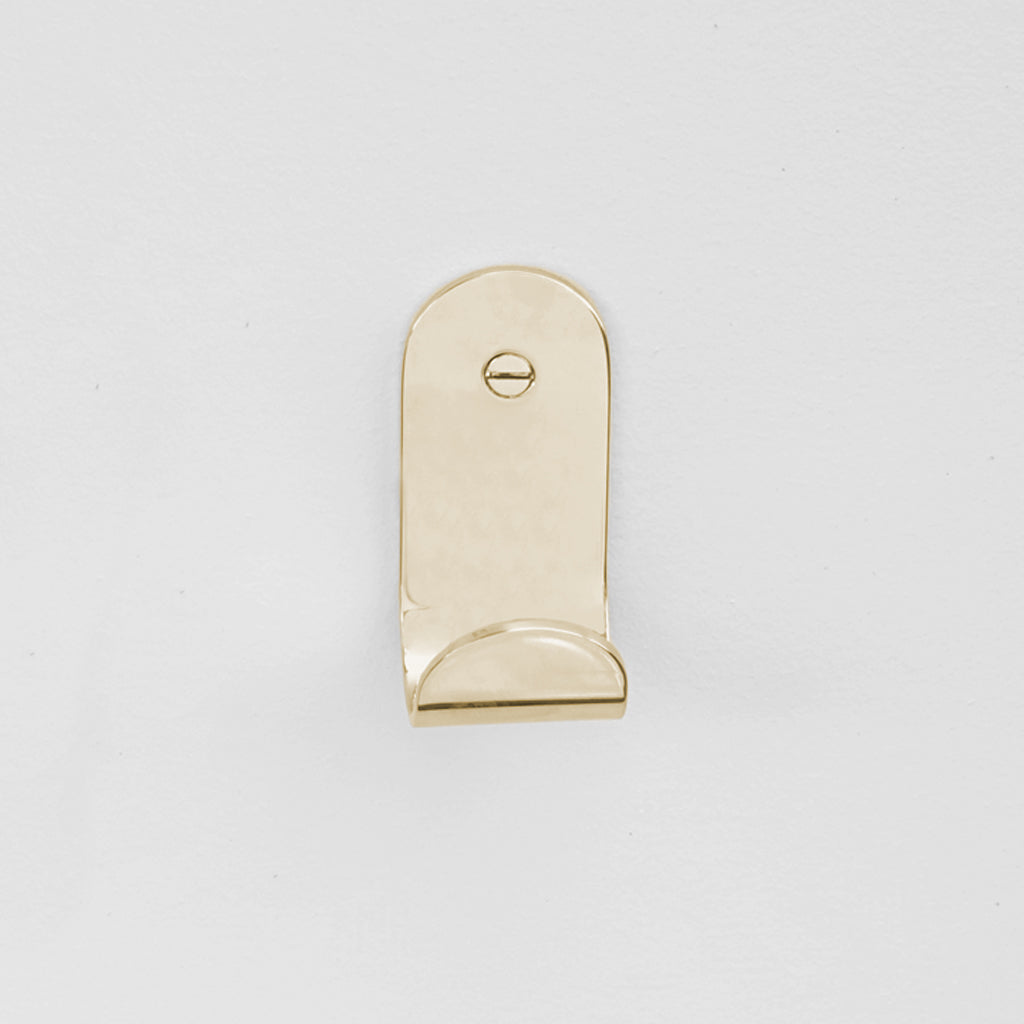 The Bende Hook 1 from CSSN in polished mirrored brass with flat head screw installed on white wall