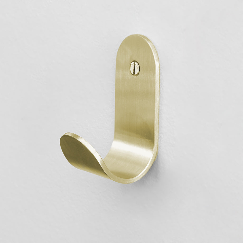 A BENDE Curve Hook door handle in gold by CSSN on a white wall.