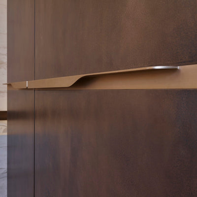 Elegant brass furniture pull handle on wood door seen on an angle. Beautifully and functionally designed.