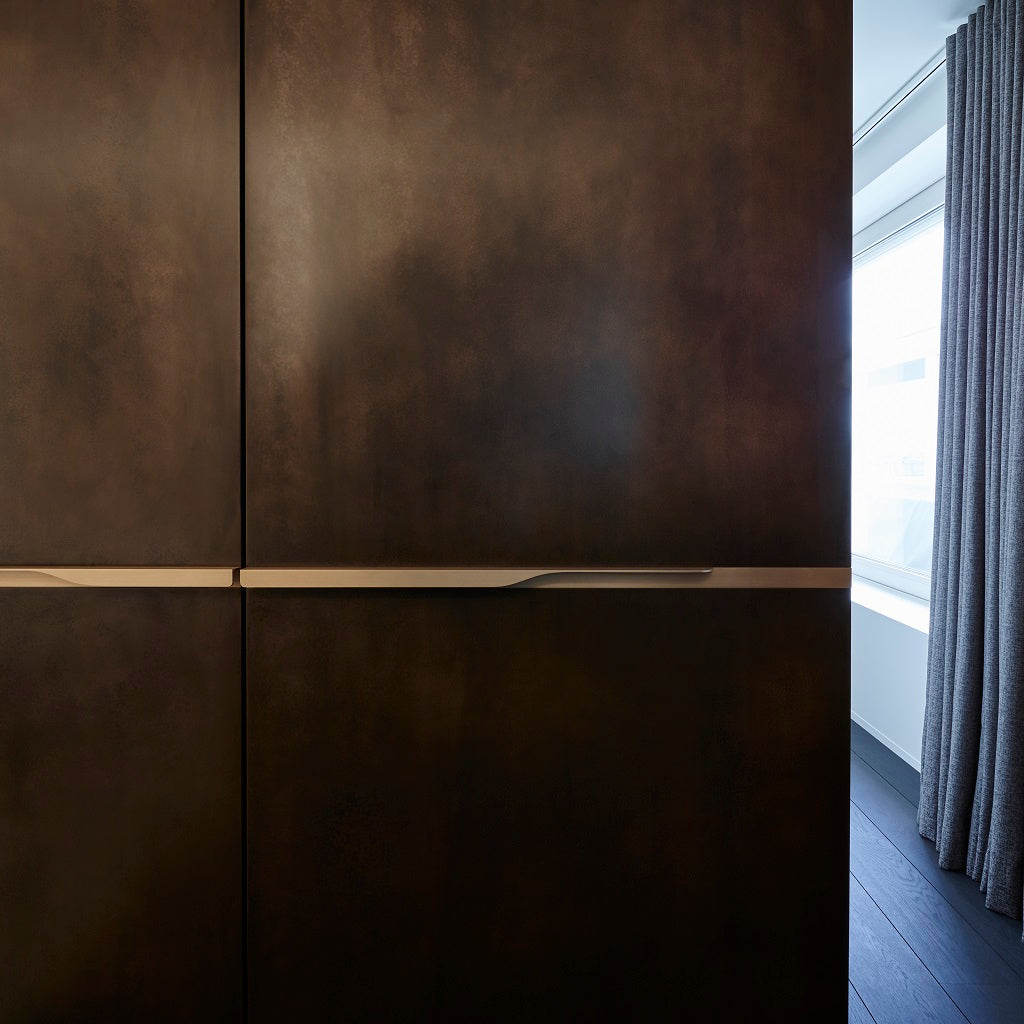 Minimal brass furniture pull handle on wood door from the front. Beautifully and functionally designed.