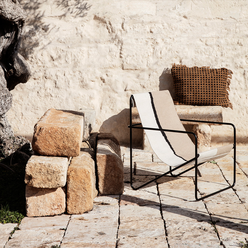 A Ferm Living Black Soil Desert Lounge Chair sitting next to a stone wall.