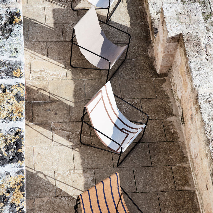 A couple of Ferm Living's Black Soil Desert Lounge Chairs sitting on top of a stone floor.