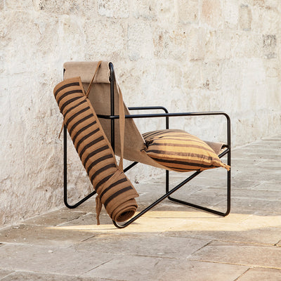 A Black Solid Desert Lounge Chair by Ferm Living with a pillow and a blanket on it.