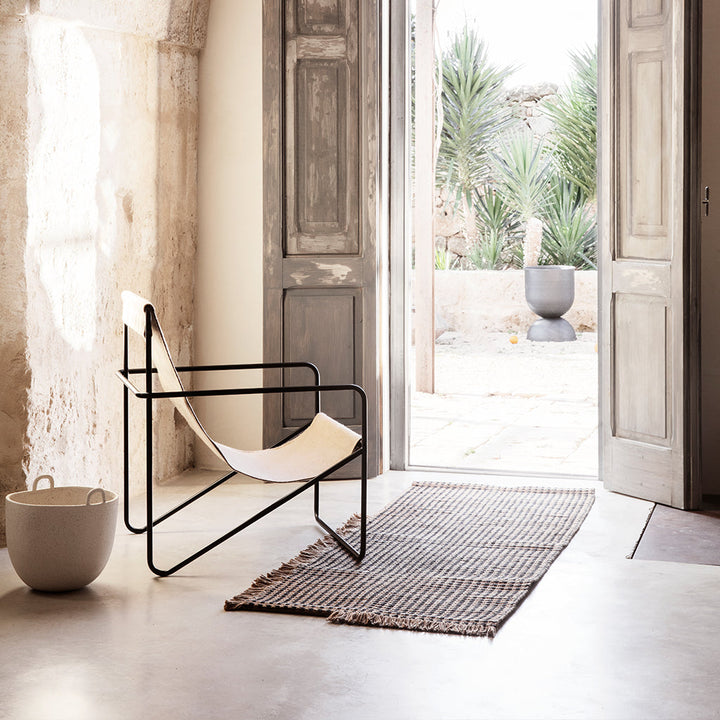 A Ferm Living Black Solid Desert Lounge Chair sitting in a room next to a door.