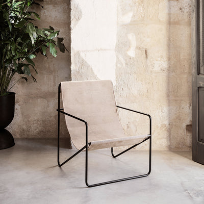 A Black Solid Desert Lounge Chair by Ferm Living sitting next to a potted plant.