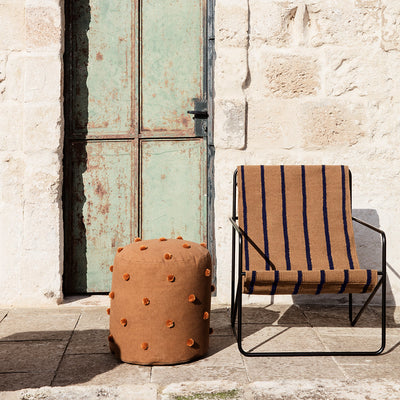 A Ferm Living Black Stripe Desert Lounge Chair and a stool sitting outside of a building.
