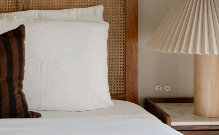 Bedroom with wooden cane headboard, white pillows, and a lamp on a nightstand with beautiful discrete flush outlets. 
