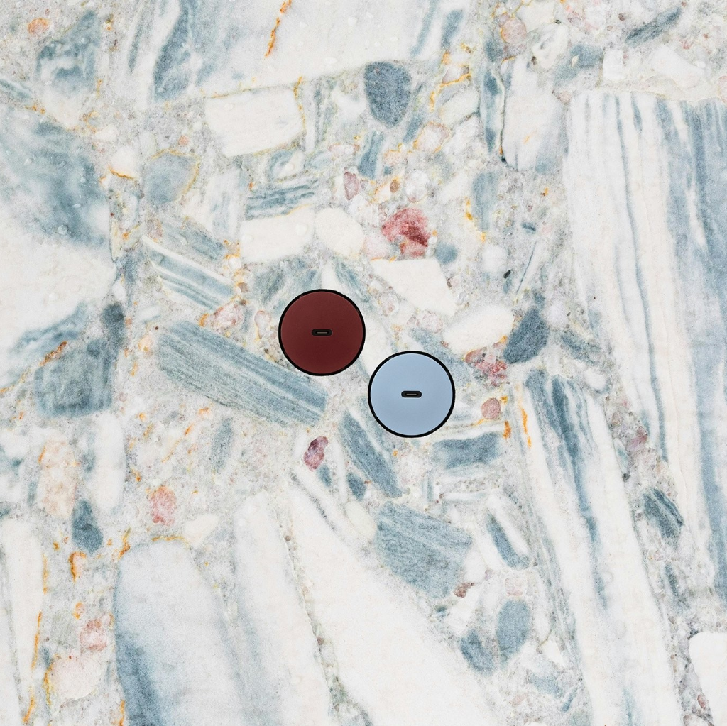 Two colorful Bocci 22 Flush Outlets in Oxblood Red and Ice Blue are set diagonally in a Terrazzo stone backsplash wall. 