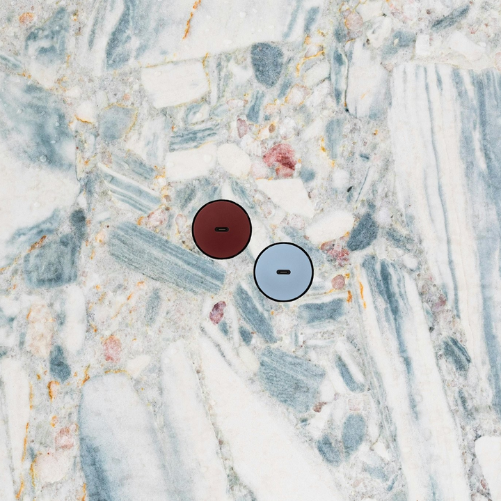 Two colorful Bocci 22 Flush Outlets in Oxblood Red and Ice Blue are set diagonally in a Terrazzo stone backsplash wall. 