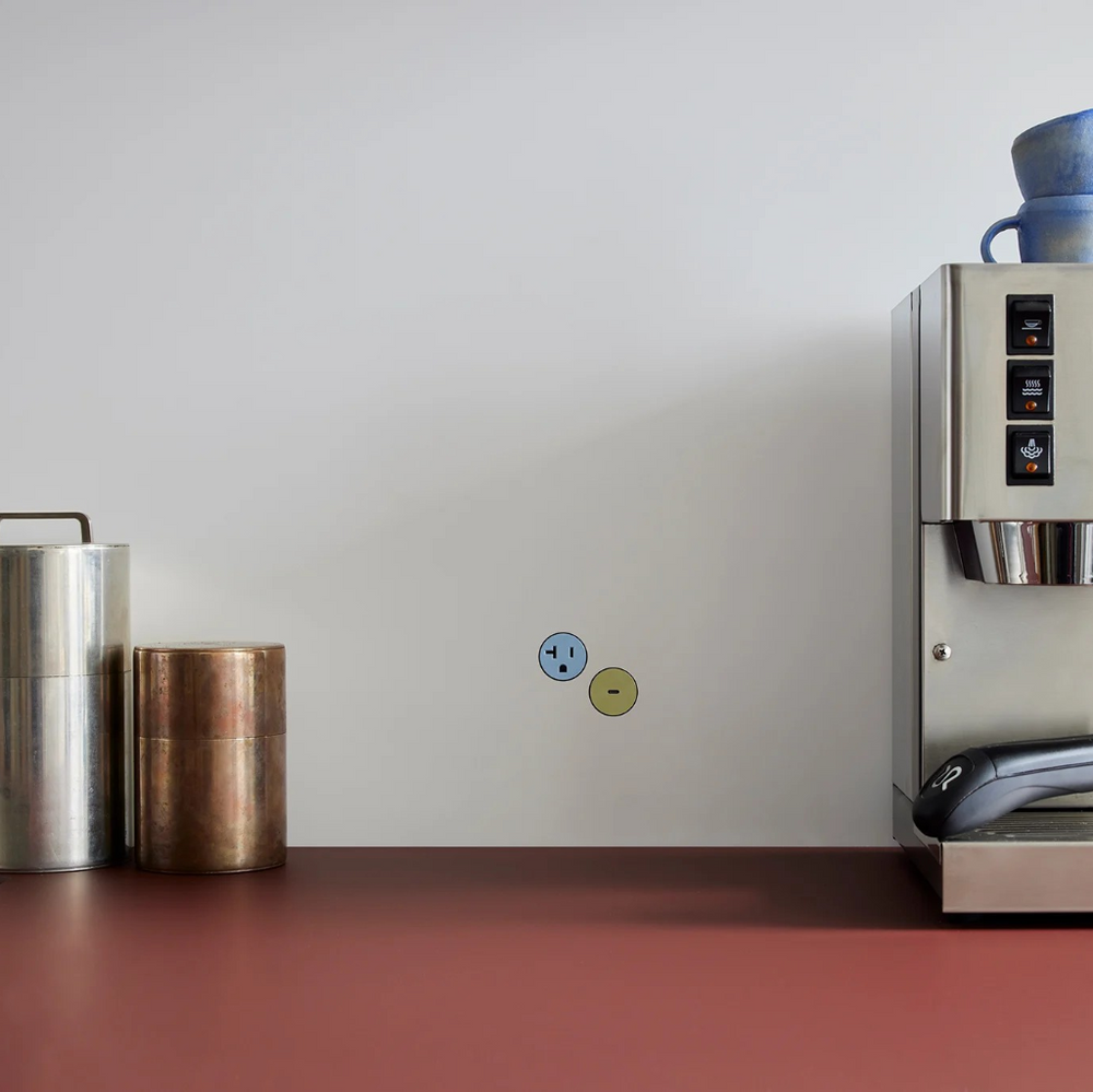 Coffee machine on a red counter surface with a white wall background with colorful Flush Bocci Plug outlets