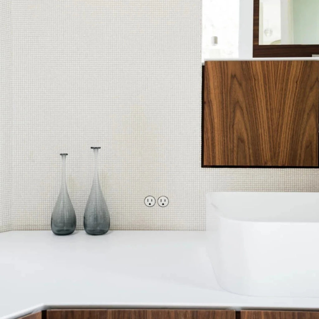An electrical outlet mounted flush into a mosaic tile surface in a bathroom. 